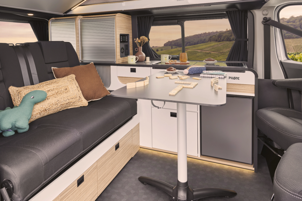 Intérieur d'un van aménagé pilot avec banquet fixe, table, et cuisine